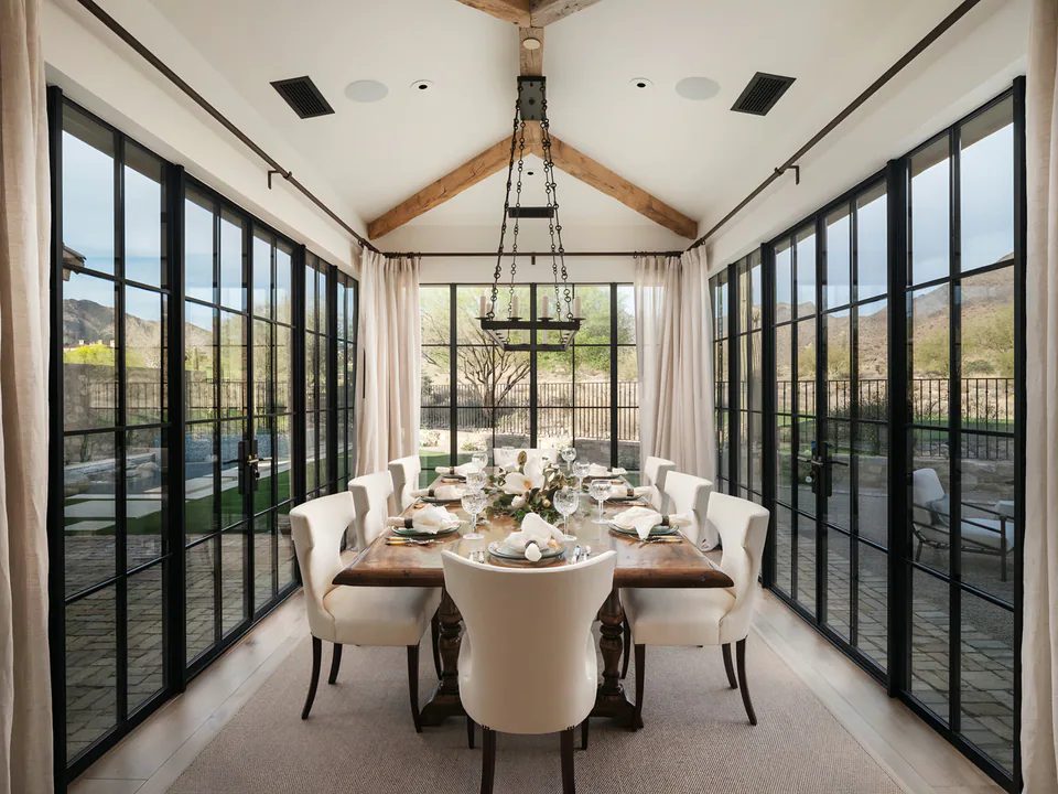 Dining room between walls of steel-framed glass, under a beamed ceiling, at The Village of Silverleaf, North Scottsdale, interior design by Paul Lauren Designs